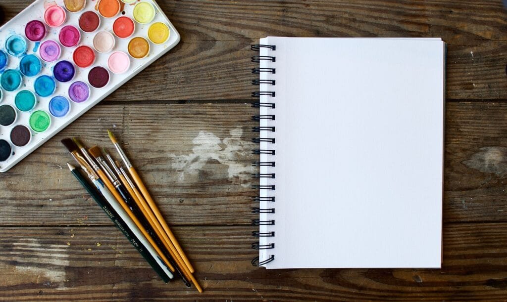 caderno em branco com conjunto de pinceis e aguarelas